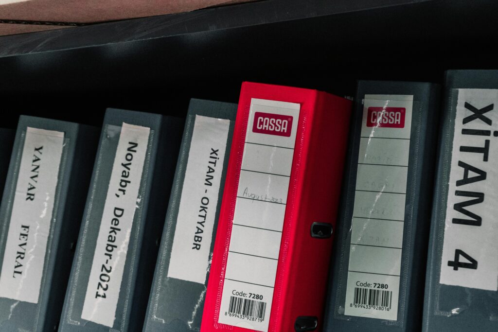 Color-coded office binders organized neatly in a storage shelf, featuring labels and a striking red binder.