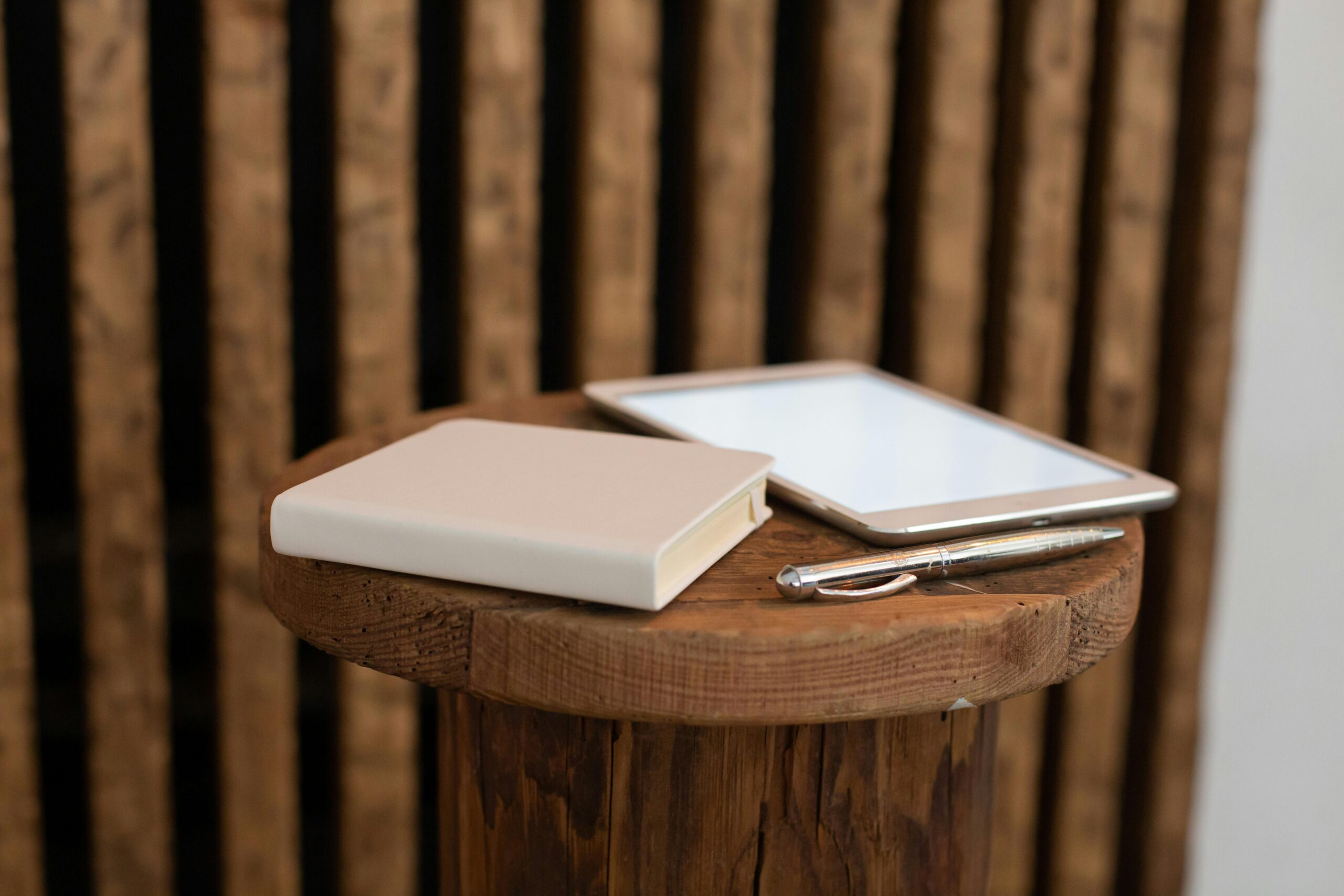 Modern workspace setup with a tablet, notebook, and pen on a wooden table.